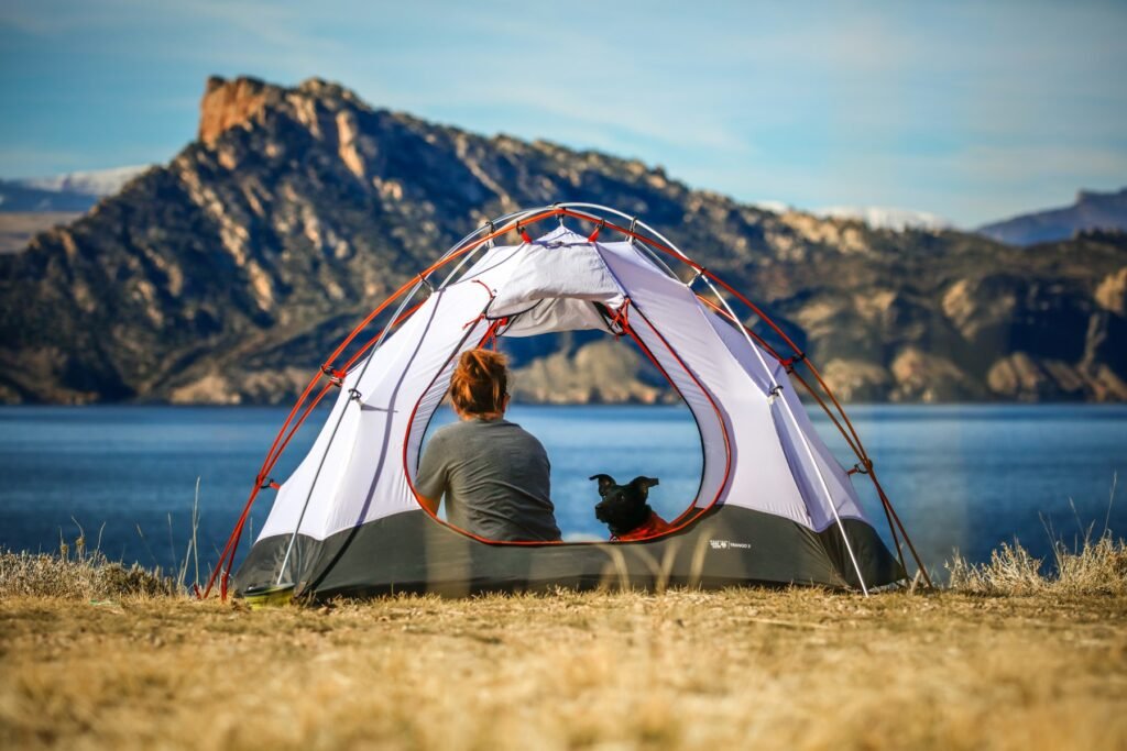 Camper and dog sitting in an open tent beside a lake