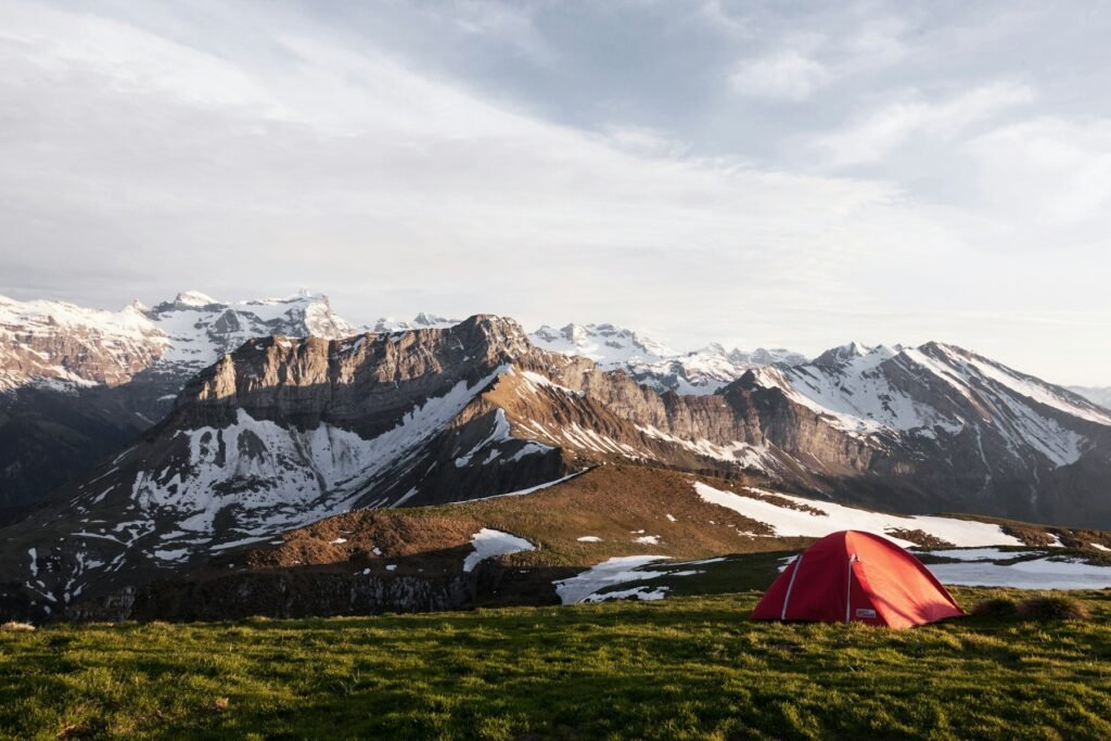 Red tent pitched on a grassy ridge below snow-capped mountains