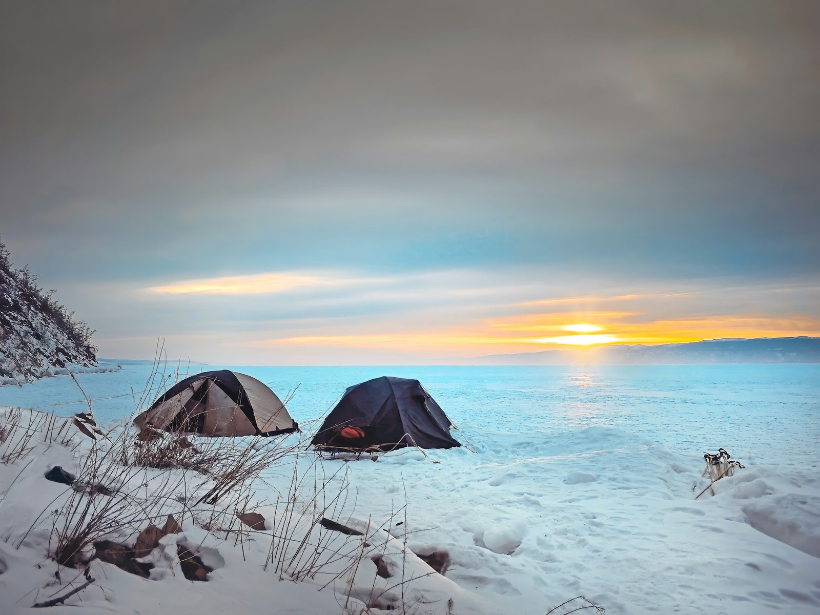 Dark tent pitched on snow at sunset